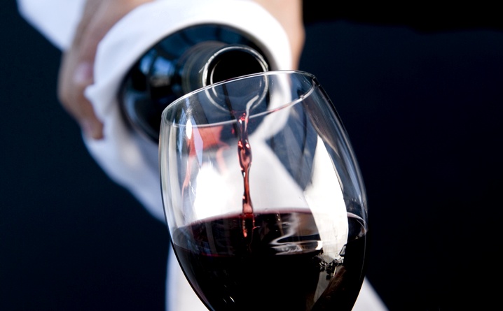 Close up of a waiter hands holding a bottle and pouring red wine in a glass